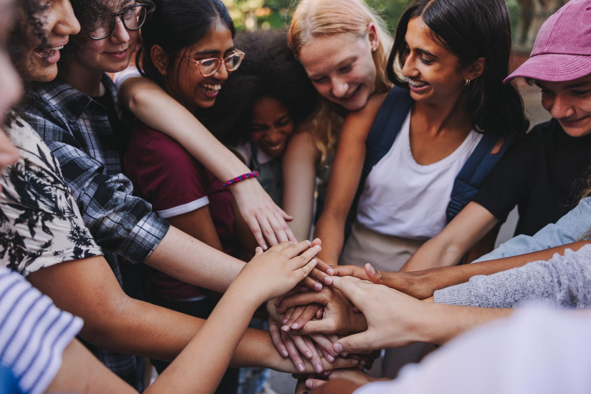 Cheerful teenagers putting their hands together in unity